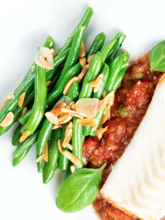 Overhead garlic green beans served on a white plate garnished with almonds.