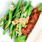 Overhead garlic green beans served on a white plate garnished with almonds featuring a title overlay.