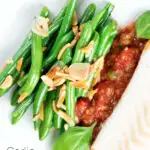 Overhead garlic green beans served on a white plate garnished with almonds featuring a title overlay.