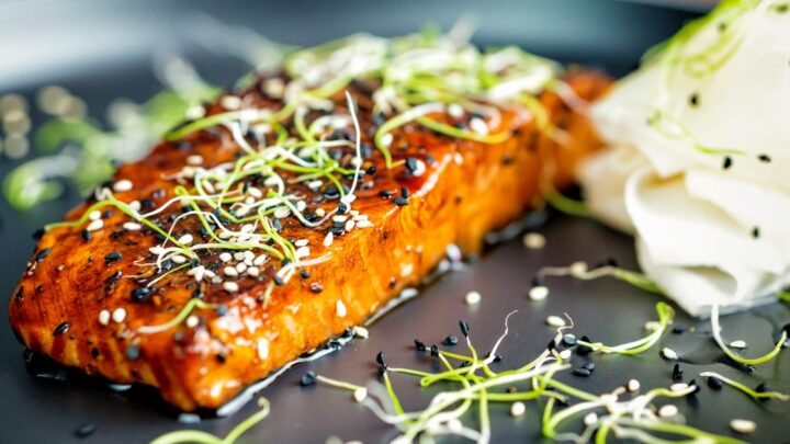 Honey soy salmon served on a black plate with pickled daikon and onion sprouts.