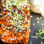Close up honey soy salmon served on a black plate with pickled daikon and onion sprouts.