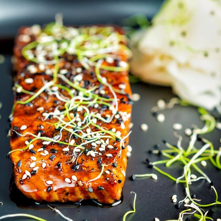 Honey soy salmon served on a black plate with pickled daikon and onion sprouts.