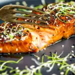 Honey soy salmon served on a black plate showing internal texture featuring a title overlay.