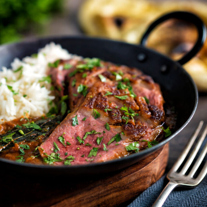 Indian duck curry served in an iron karai with rice and naan bread.