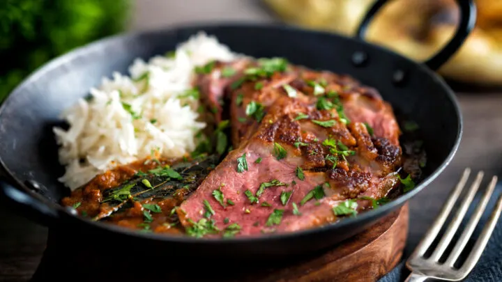 Indian duck breast curry served in an iron karai with rice and naan bread.