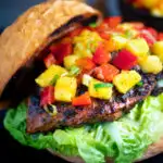 Jamaican jerk chicken burger with a mango salsa served on a toasted bun featuring a title overlay.