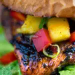 Close up Jamaican jerk chicken burger with a mango salsa featuring a title overlay.