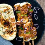 Overhead lamb tikka kebabs with onion and green pepper served with a naan bread.