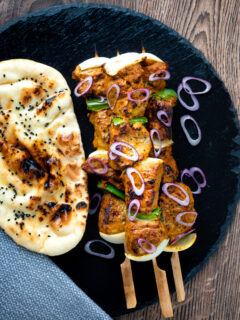 Overhead lamb tikka kebabs with onion and green pepper served with a naan bread.