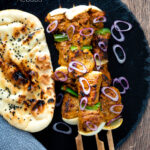 Overhead lamb tikka kebabs with onion and green pepper served with a naan bread featuring a title overlay.