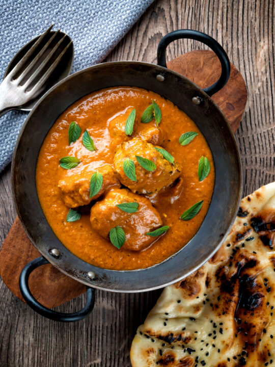 Overhead Indian lamb tikka masala curry served with a naan bread.