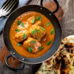 Overhead Indian lamb tikka masala curry served with a naan bread featuring a title overlay.