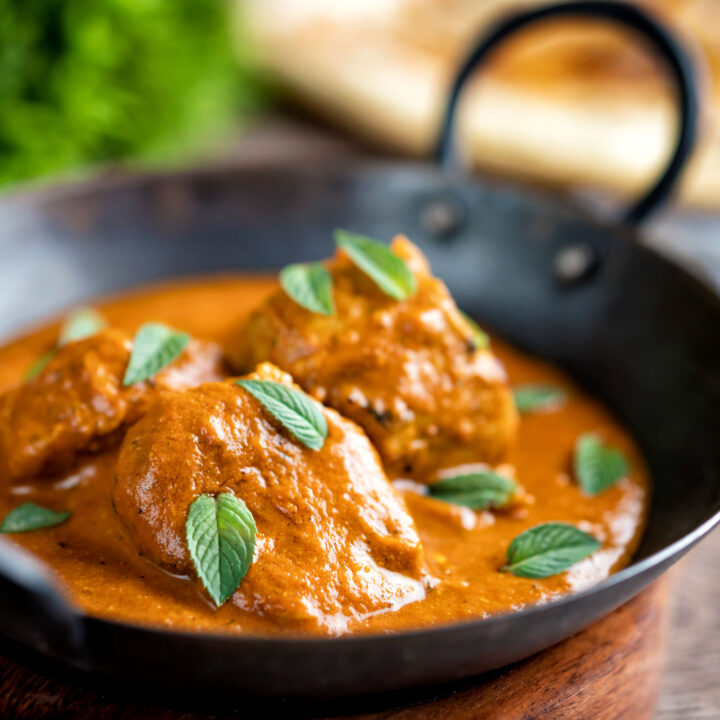 Indian lamb tikka masala curry served peppermint leaves in an iron bowl.