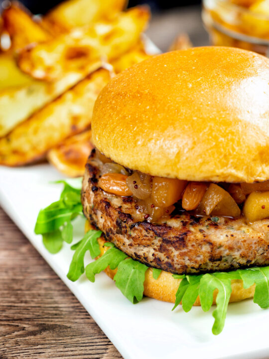 Pork and apple burgers served with rocket, chutney and a side of potato wedges.