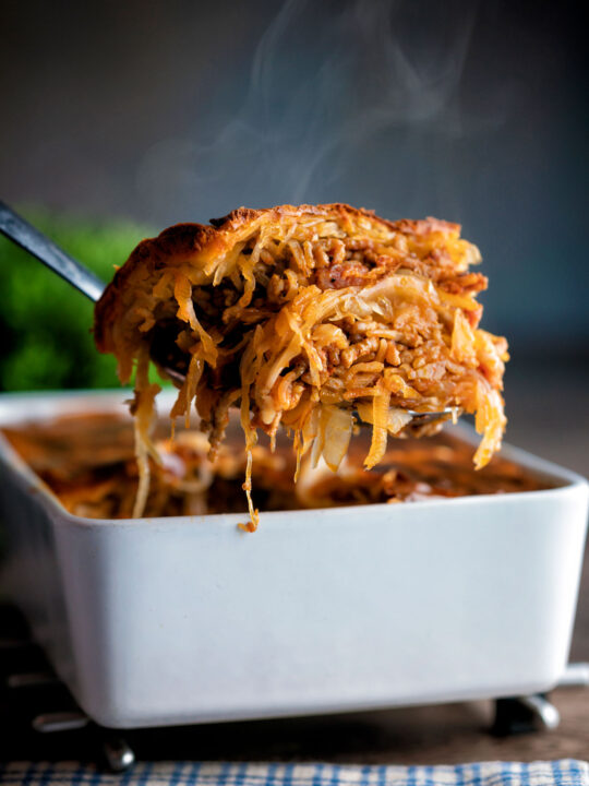 Steaming hot rakott kaposzta, Hungarian sauerkraut casserole being removed from a bowl.