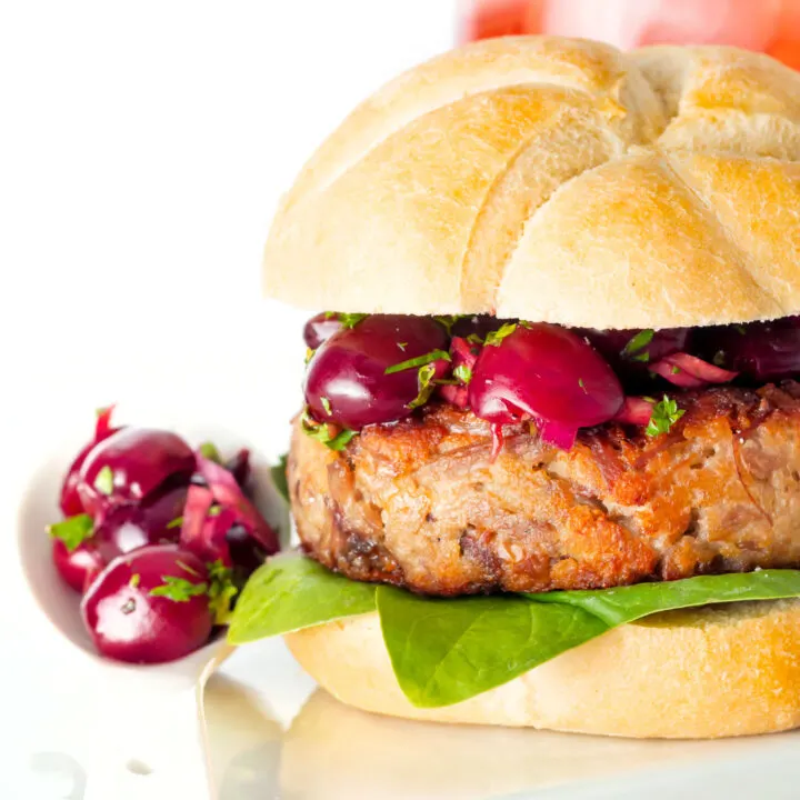 Close up shredded duck burgers topped with cherry salsa on a burger bun.