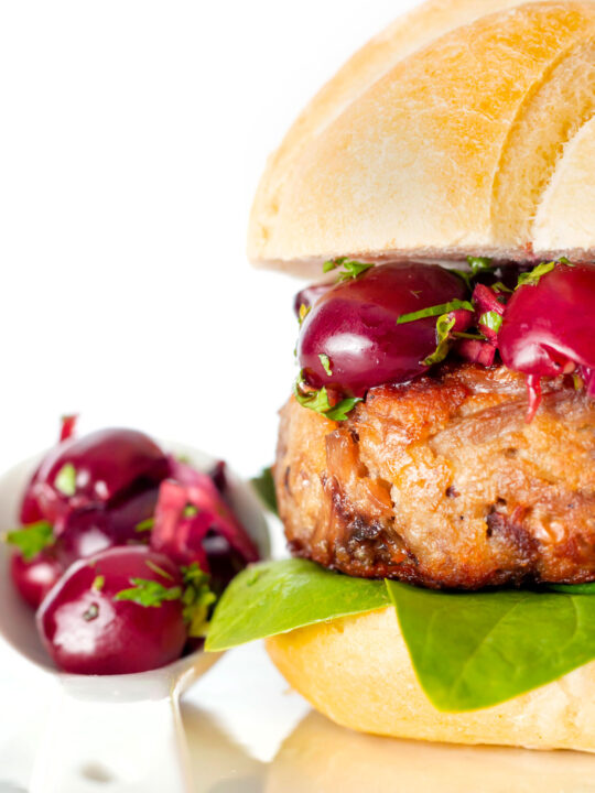 Shredded duck burgers topped with cherry salsa on a burger bun.