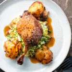 Overhead slow roast duck leg with balsamic gravy, cabbage and roast potatoes.