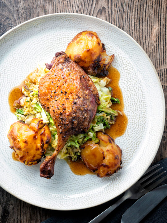 Overhead slow roast duck leg with balsamic gravy, cabbage and roast potatoes.