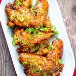 Overhead sticky spicy Thai inspired chicken wings with green onion featuring a title overlay.