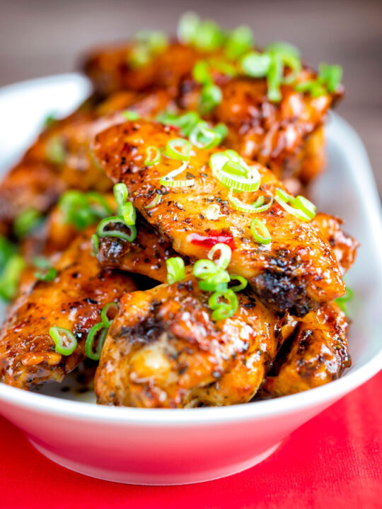 Sticky spicy Thai inspired chicken wings with green onion served in a white bowl.