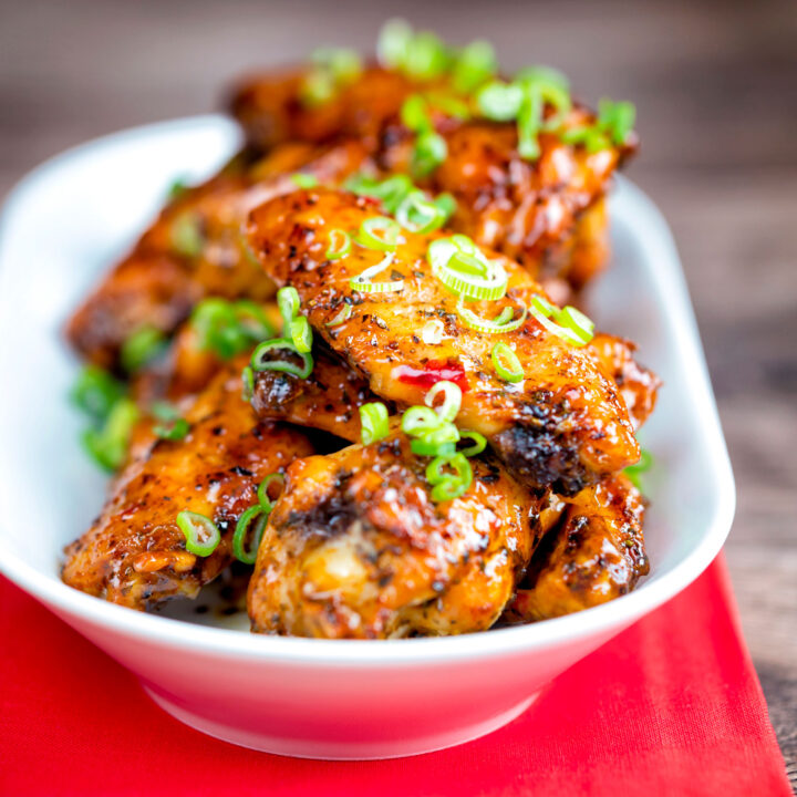 Sticky spicy Thai inspired chicken wings with green onion served in a white bowl.