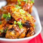 Close up sticky spicy Thai inspired chicken wings with green onion.