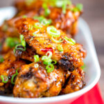 Close up sticky spicy Thai inspired chicken wings with green onion featuring a title overlay.