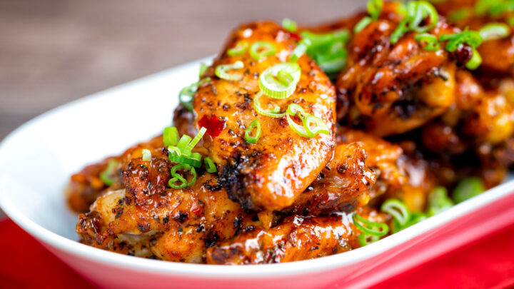 Sticky spicy Thai chicken wings with green onion served in a white bowl.