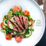 Overhead Thai beef salad with rare beef, tomatoes, mint, chilli and cucumber featuring a title overlay.
