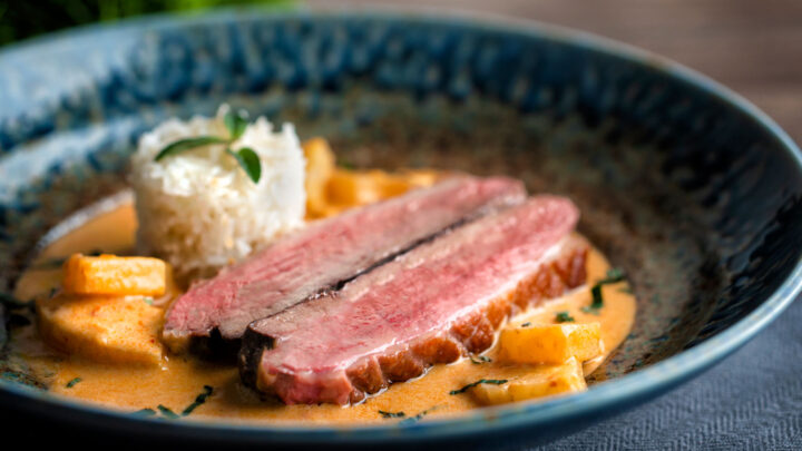 Thai red duck curry with pineapple, rice and Thai basil in a blue bowl.