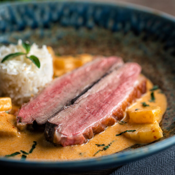 Thai red duck curry with pineapple, rice and Thai basil in a blue bowl.