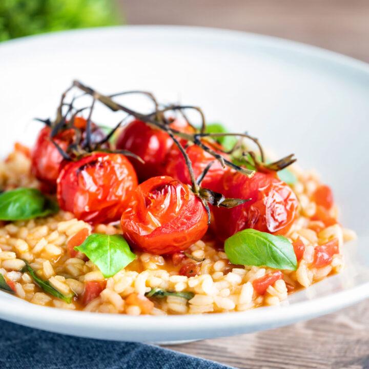 Tomato risotto with basil and balsamic roasted tomatoes served in a white bowl.