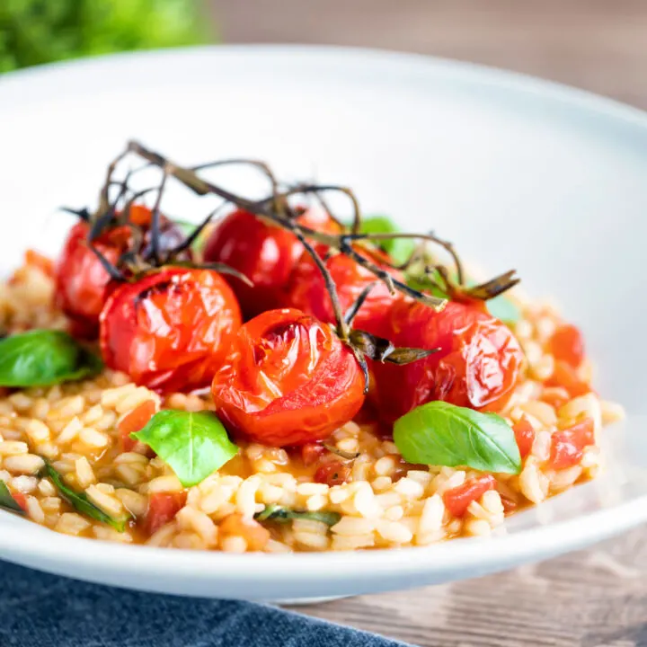 Tomato risotto with basil and balsamic roasted tomatoes served in a white bowl.