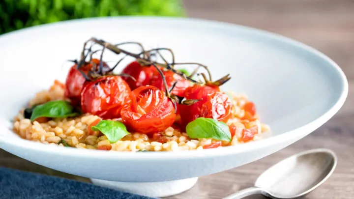 Tomato risotto with basil and balsamic roasted tomatoes served in a white bowl.