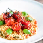 Tomato risotto with basil and roasted tomatoes served in a white bowl.