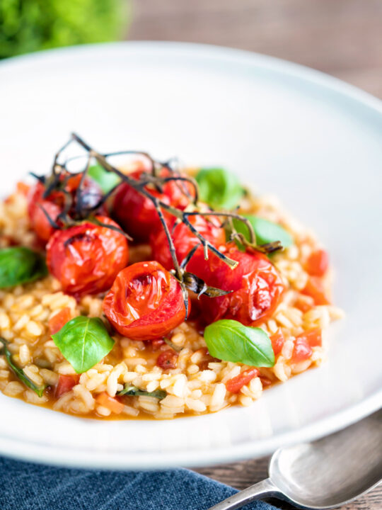 Tomato risotto with basil and roasted tomatoes served in a white bowl.