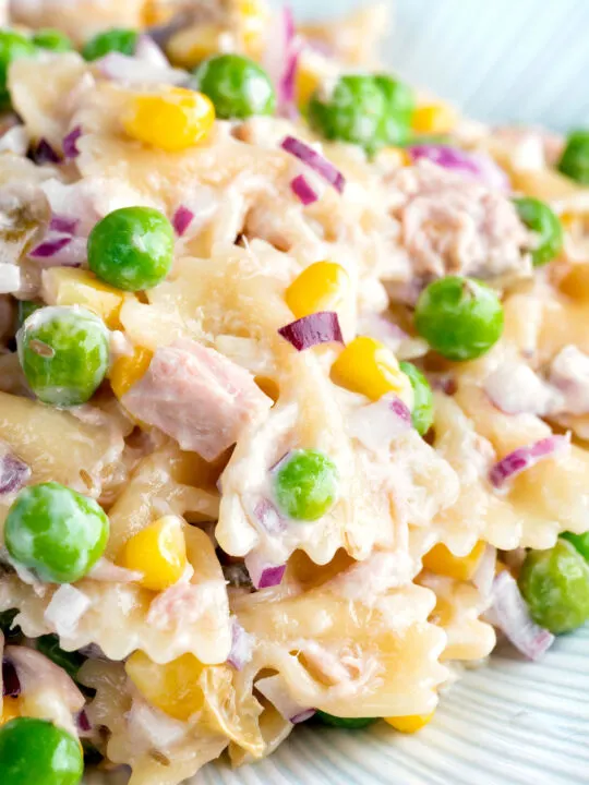 Close up tuna pasta salad with peas, corn and red onion.