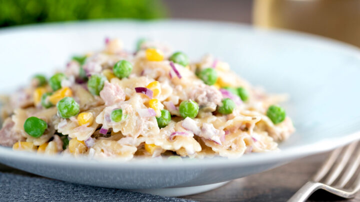 Tuna pasta salad with peas, corn and red onion served in a white bowl.