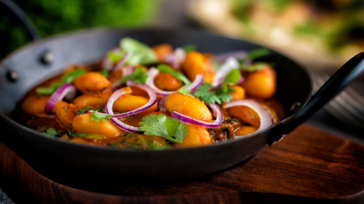 Indian vegan butter bean curry served with coriander, red onion in a kadai.