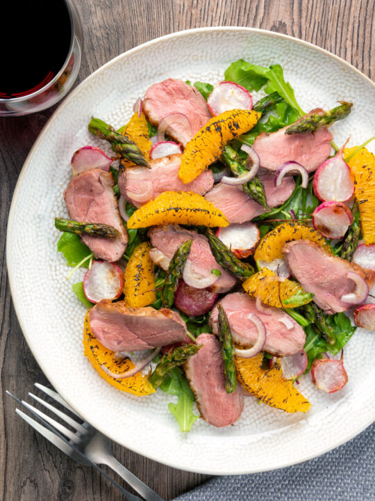 Overhead duck breast salad with roasted radish and asparagus with orange segments.