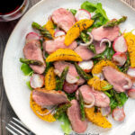 Overhead duck breast salad with roasted radish and asparagus with orange segments featuring a title overlay.