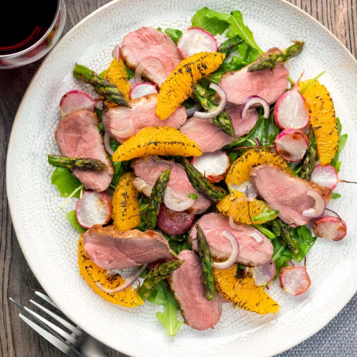 Overhead duck breast salad with rocket, roasted radish and asparagus with orange segments.