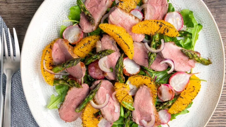 Overhead duck breast salad with rocket, roasted radish and asparagus with orange segments.