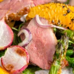 Close up duck breast salad with roasted radish and asparagus with orange segments.