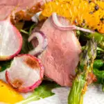 Close up duck breast salad with roasted radish and asparagus with orange segments featuring a title overlay.