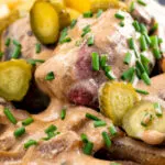 Close up beef and mushroom stroganoff served with fried potatoes and pickles.