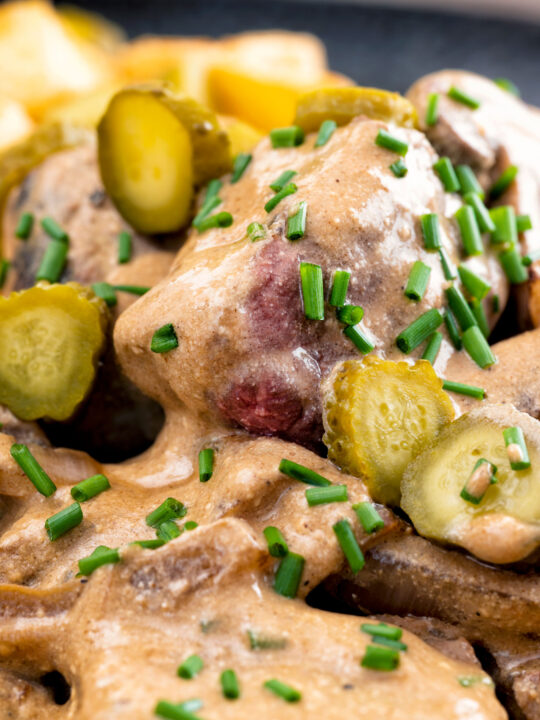 Close up beef and mushroom stroganoff served with fried potatoes and pickles.