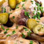 Close up beef and mushroom stroganoff served with fried potatoes and pickles featuring a title overlay.