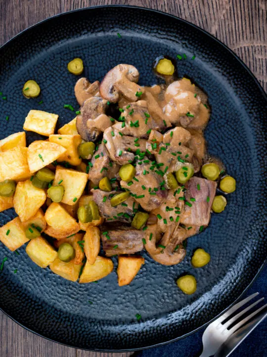 Overhead beef and mushroom stroganoff served with fried potatoes and pickles.